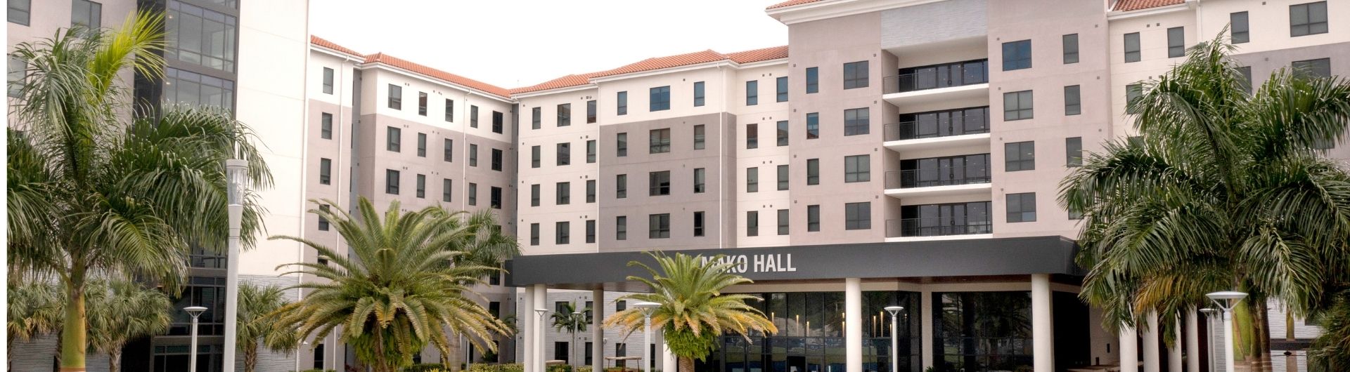 An exterior view of Mako Hall adorned by lean landscaping and healthy palms.