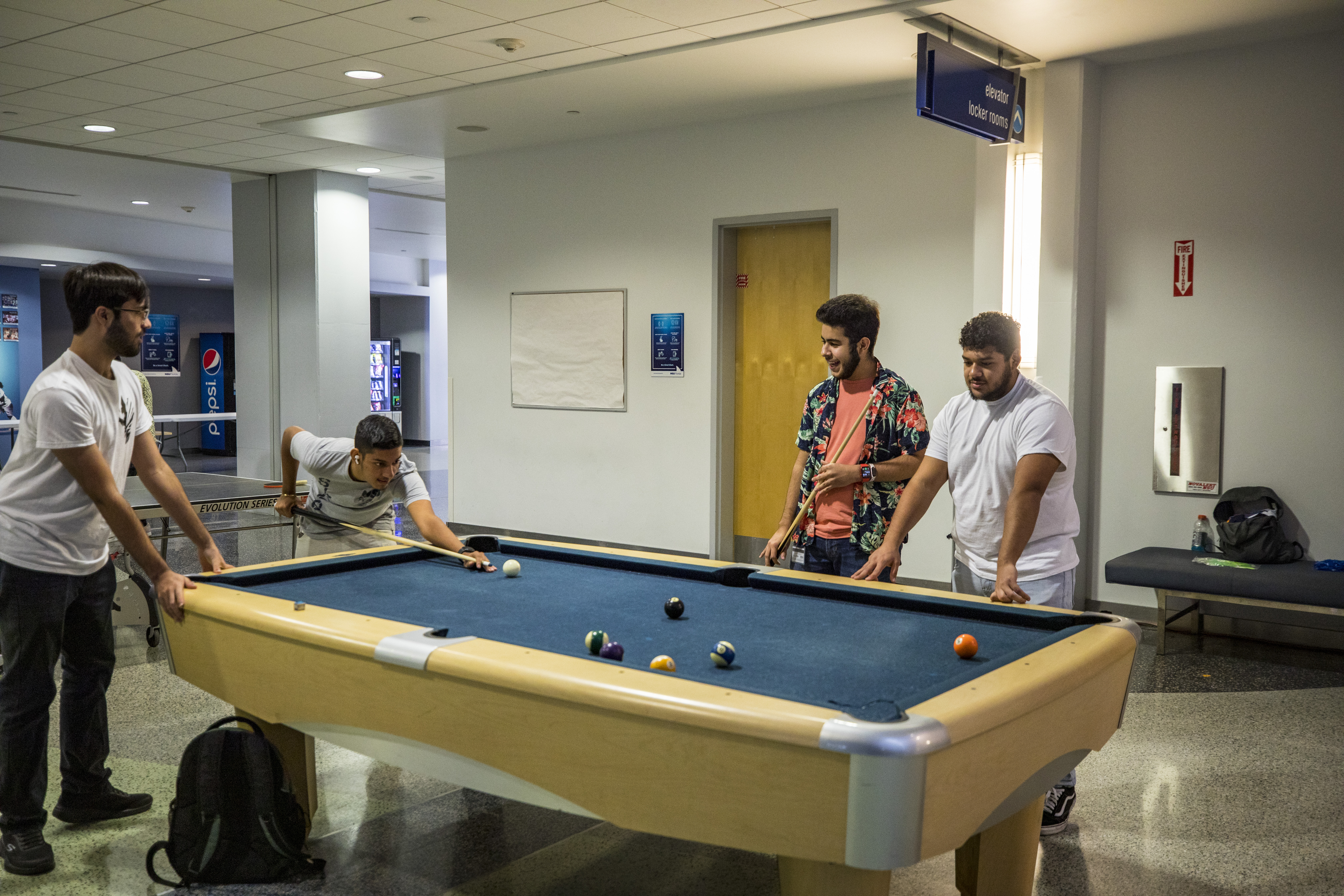 Four students gather around a pool table while one takes aim. Stripes are minimally in the lead with an advantage of one.